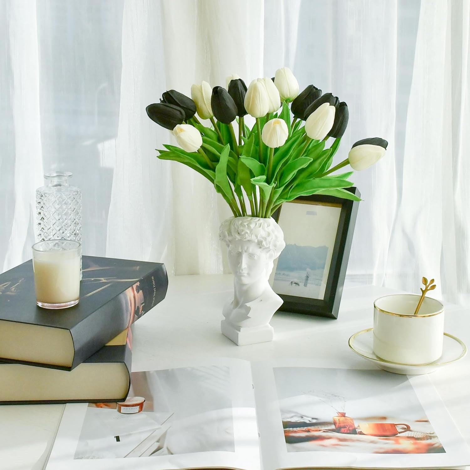 Decorative table setting with black and white tulips in a white vase, books, and a glass of milk.