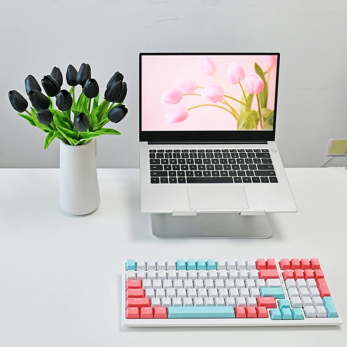Colorful keyboard on a desk with a laptop displaying flowers and a vase of black tulips.