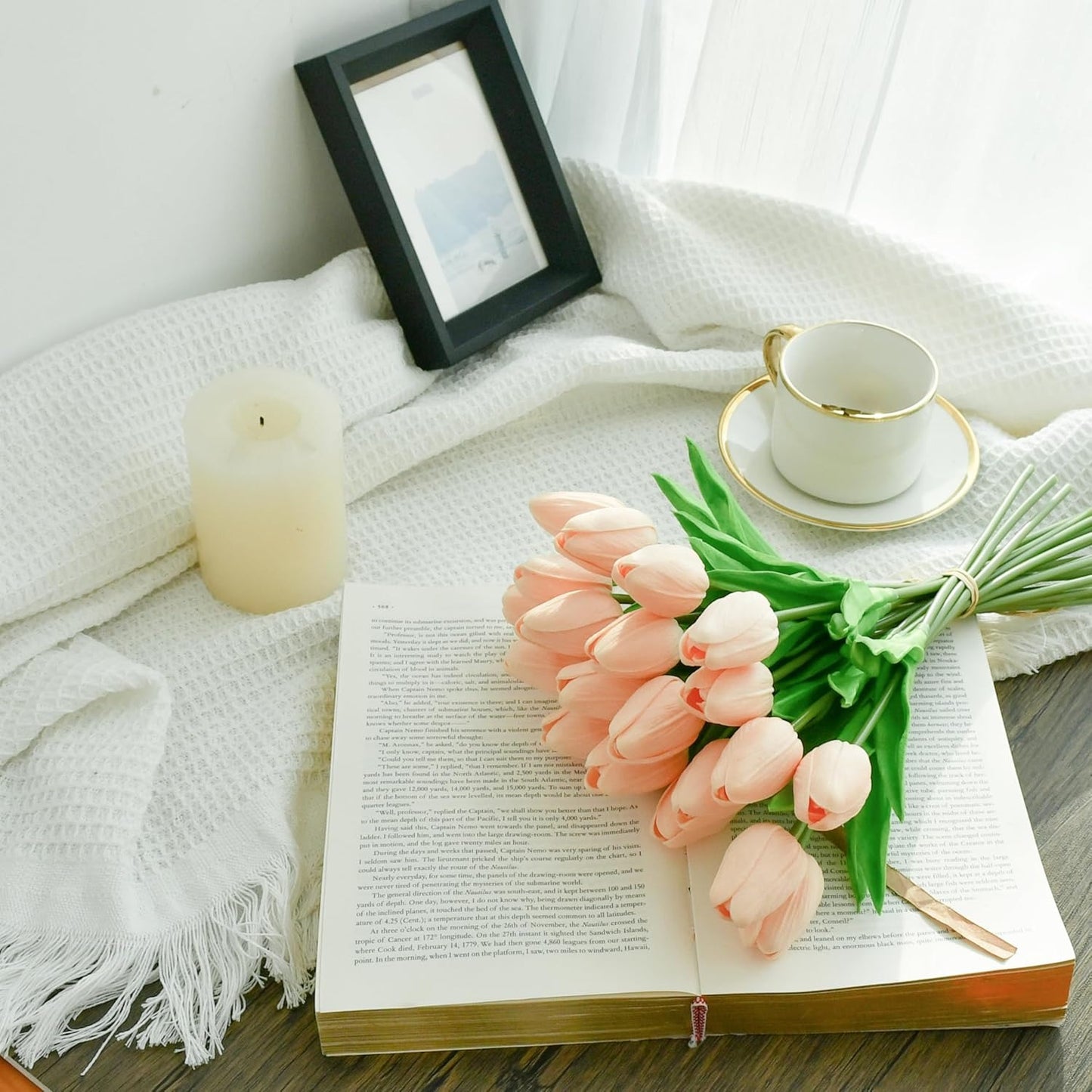 Bouquet of pink tulips on an open book with a candle and framed picture in the background.