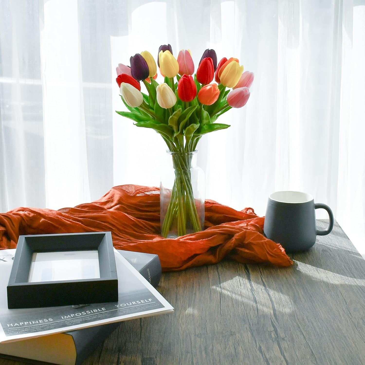 Colorful tulips in a vase on a table with a mug and framed picture.