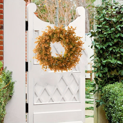 Decorative wreath on a white garden gate with greenery around