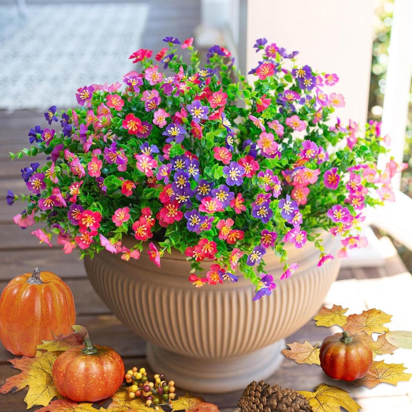 Potted plant with colorful flowers on a table with pumpkins and autumn leaves.