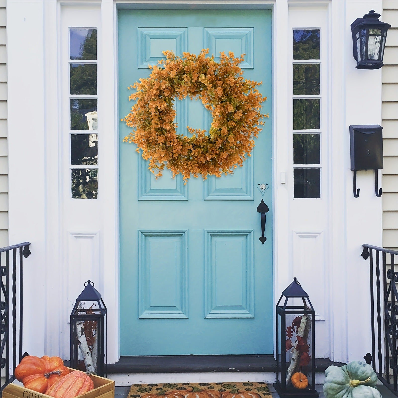 Turquoise front door with a wreath and pumpkins on a porch