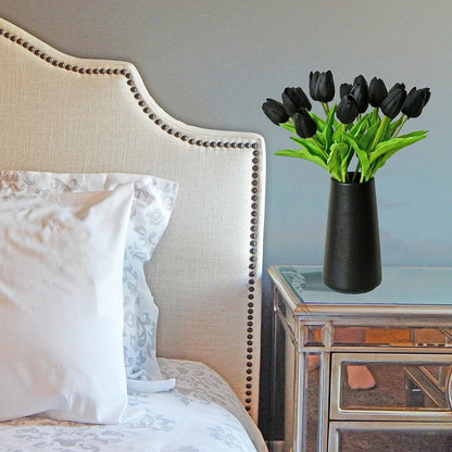 Decorative vase with black tulips on a nightstand next to a bed with white pillows.