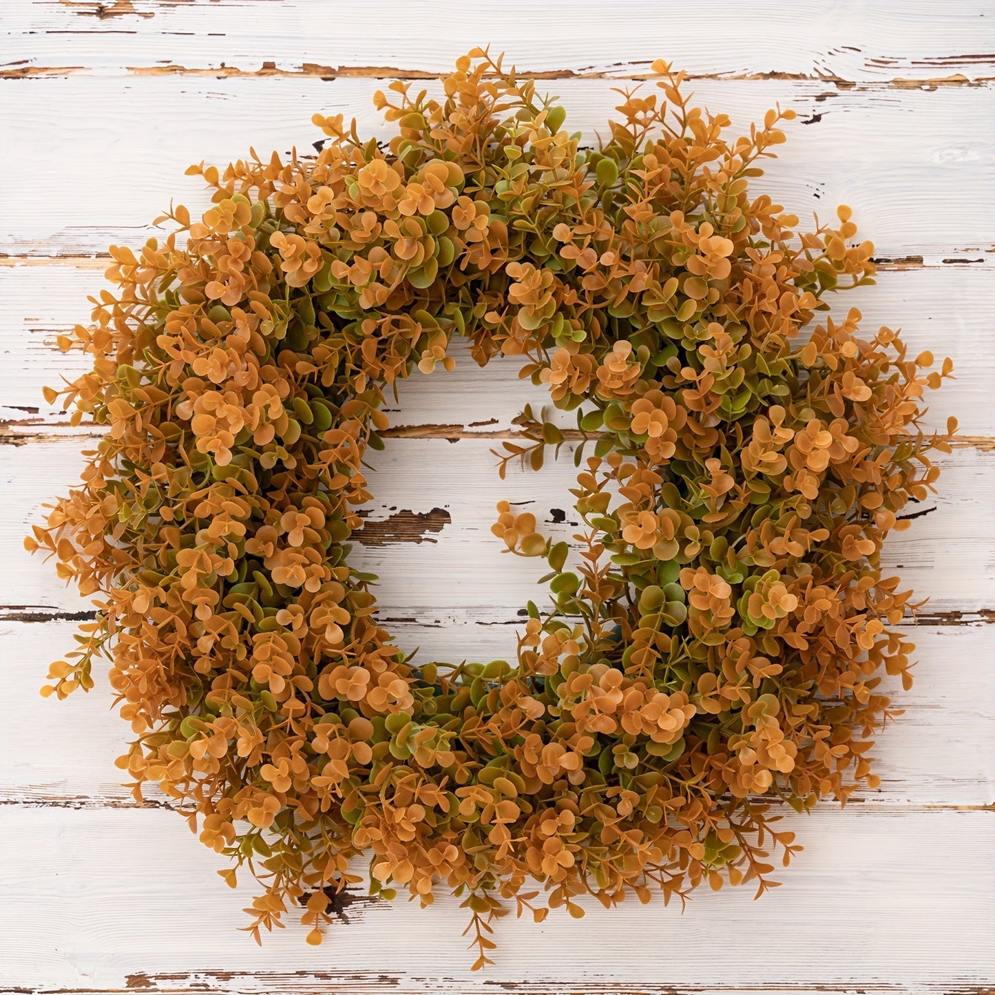 Wreath with orange and green leaves on a white wooden background