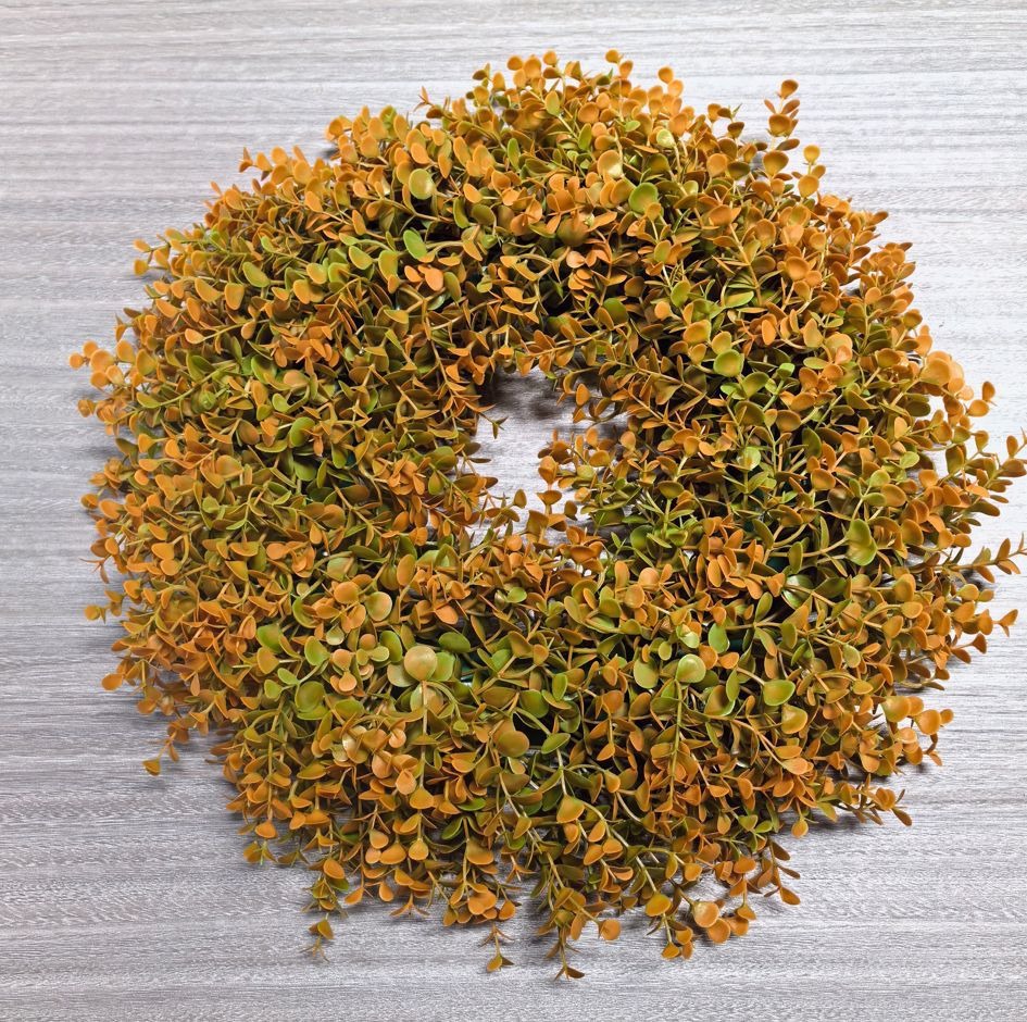 Wreath made of artificial green and orange leaves on a textured gray background